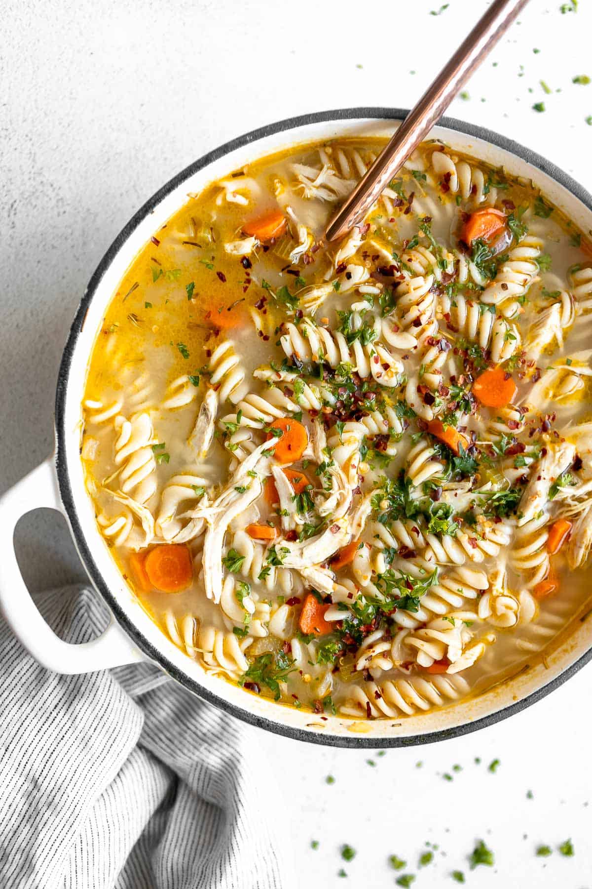 gluten free chicken noodle soup in a pot with carrots and a spoon on the side