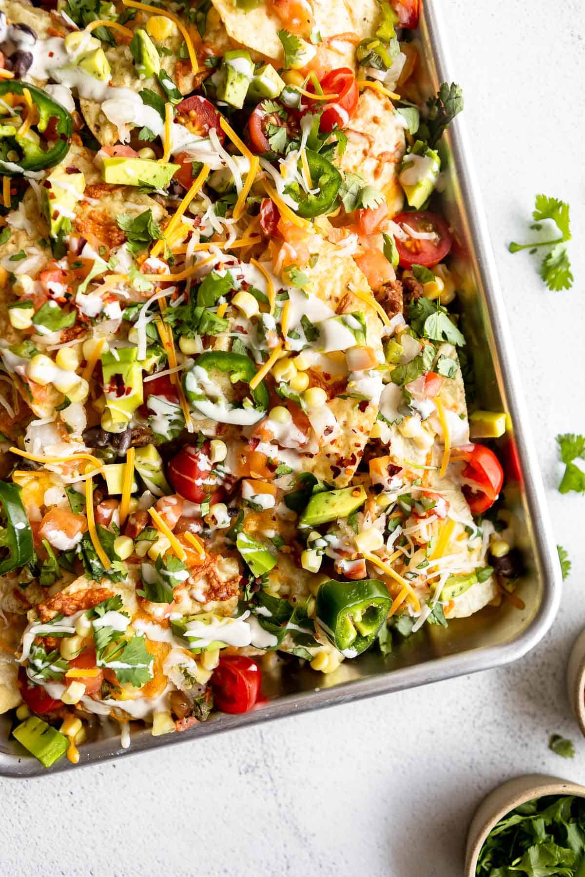 vegan and vegetarian nachos on a baking sheet with cheese and avocado